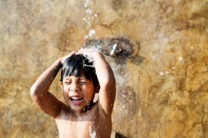 A little boy washing his body under pouring water