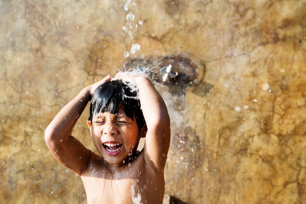 A little boy washing his body under pouring water