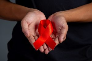 A woman's hands holding a red-ribbon symbolizing HIV awareness and care for HIV patients around the world.