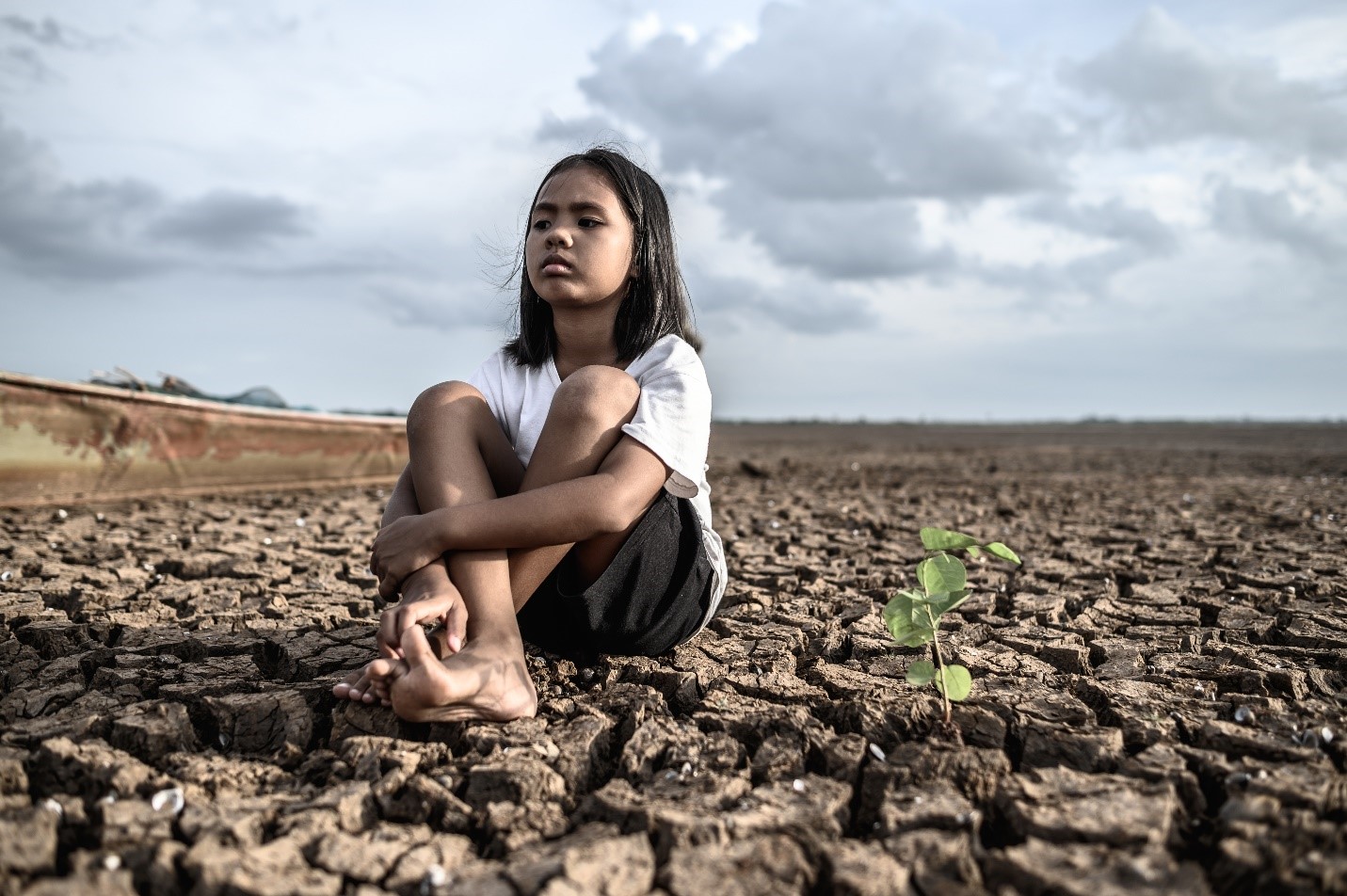 a small girl sitting on an area affected by drought